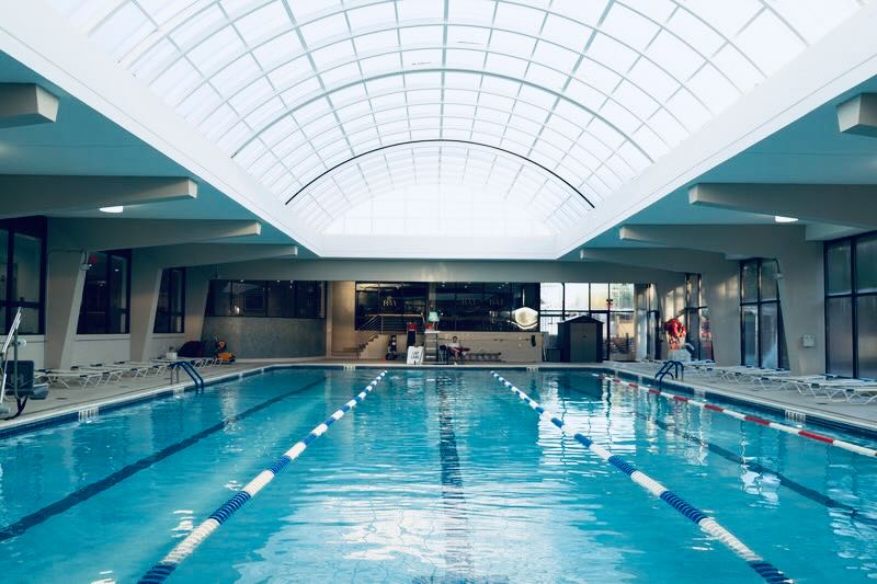Sunlit indoor lap pool with glass roof and deck chairs