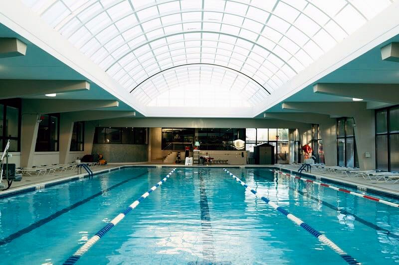 Sunlit indoor lap pool with glass roof and deck chairs